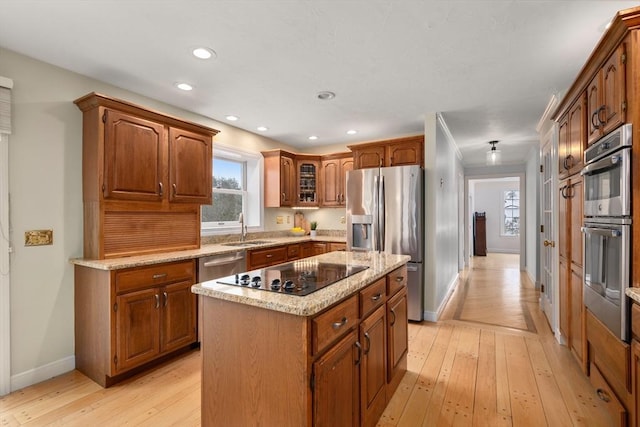 kitchen featuring light stone counters, a sink, appliances with stainless steel finishes, brown cabinets, and light wood finished floors