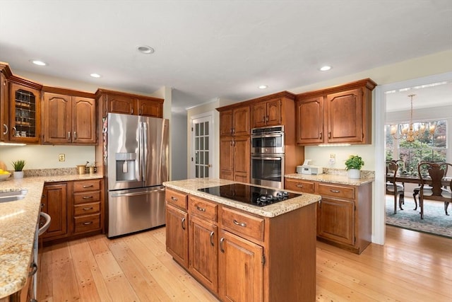 kitchen with light wood finished floors, appliances with stainless steel finishes, a kitchen island, and light stone counters