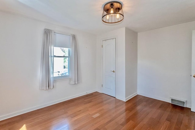 spare room featuring wood finished floors, a chandelier, and baseboards