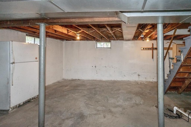 basement featuring freestanding refrigerator and stairway