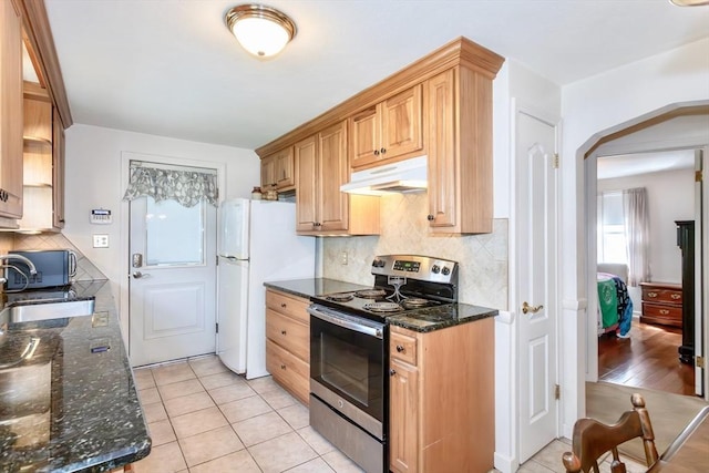 kitchen with stainless steel range with electric stovetop, under cabinet range hood, a sink, backsplash, and dark stone countertops