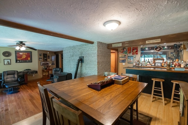 dining area with bar, ceiling fan, light hardwood / wood-style flooring, and a textured ceiling