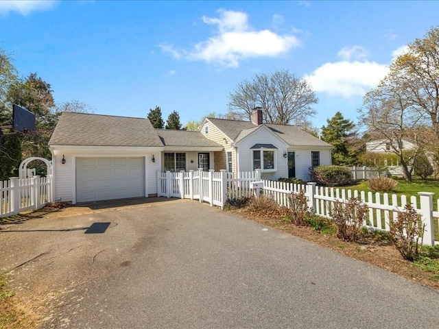 view of front of home featuring driveway, a fenced front yard, an attached garage, and a chimney
