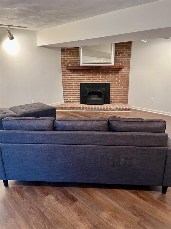 living area with a brick fireplace, a textured ceiling, baseboards, and wood finished floors