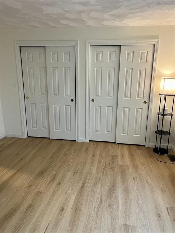 unfurnished bedroom with light wood-style floors, baseboards, and multiple closets