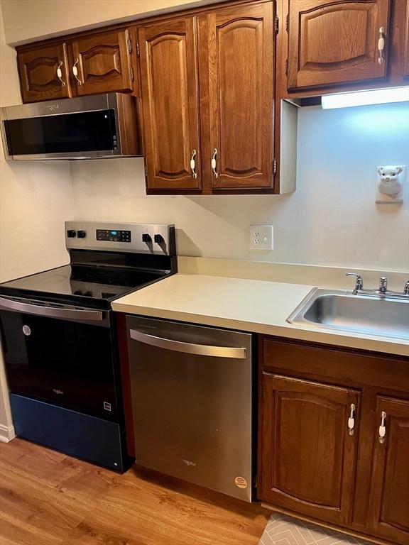 kitchen with stainless steel appliances, light wood-style flooring, a sink, and light countertops