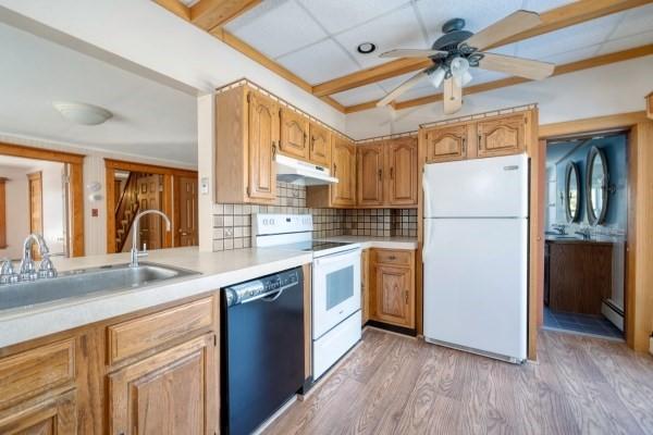 kitchen featuring under cabinet range hood, a baseboard heating unit, white appliances, a sink, and light countertops