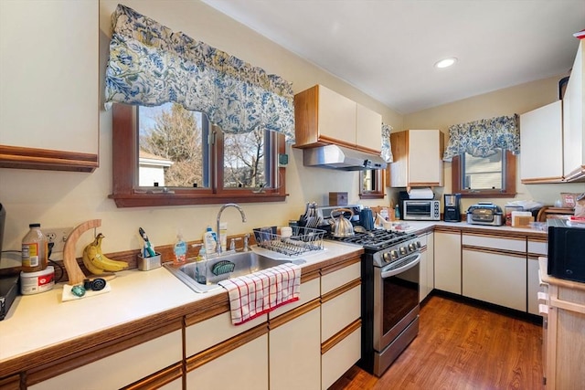 kitchen with stainless steel gas range oven, under cabinet range hood, a sink, light wood-style floors, and white cabinets