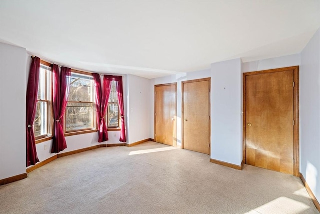 unfurnished bedroom featuring carpet, baseboards, and two closets