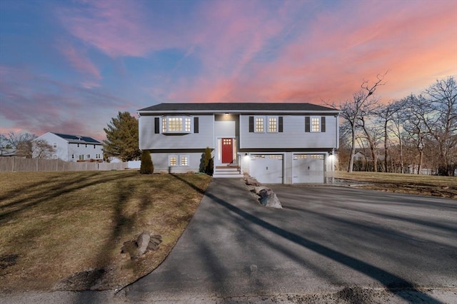 split foyer home featuring entry steps, aphalt driveway, an attached garage, fence, and a yard