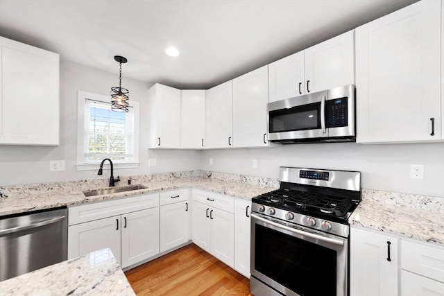 kitchen featuring stainless steel appliances, white cabinets, a sink, and light wood finished floors