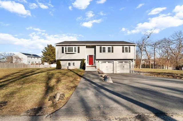 bi-level home with aphalt driveway, a front lawn, fence, and a garage