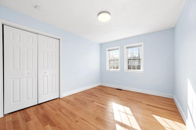 unfurnished bedroom featuring light wood-type flooring, a closet, visible vents, and baseboards