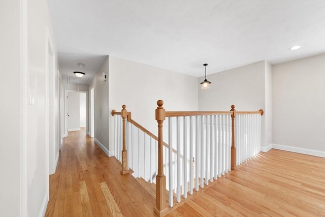 hallway with attic access, baseboards, light wood-style floors, and an upstairs landing