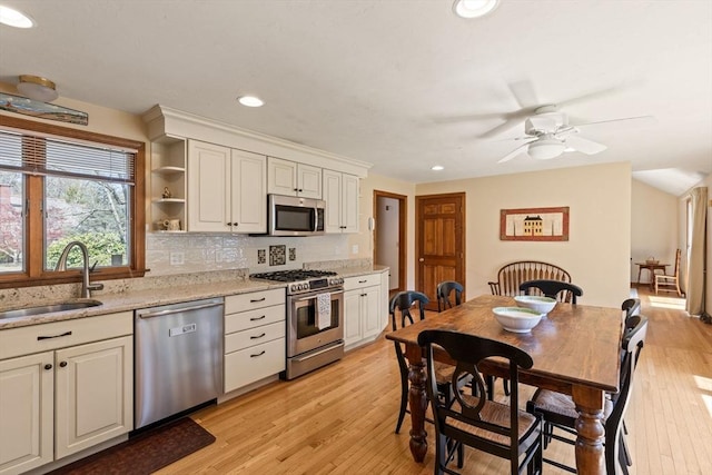 kitchen with ceiling fan, appliances with stainless steel finishes, a sink, light wood finished floors, and tasteful backsplash