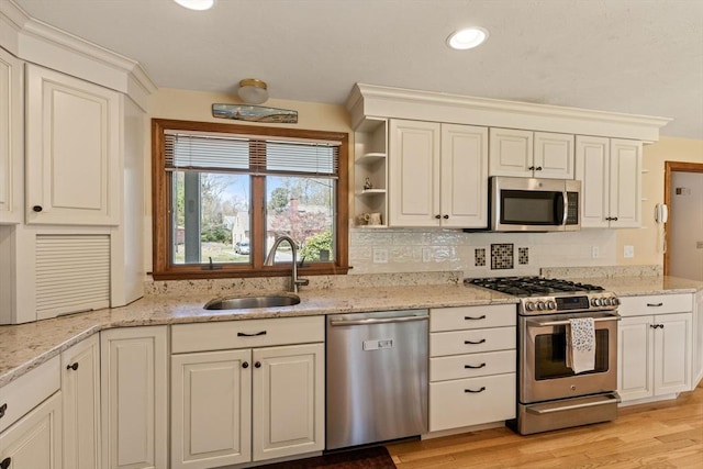 kitchen with backsplash, appliances with stainless steel finishes, light stone countertops, light wood-type flooring, and a sink