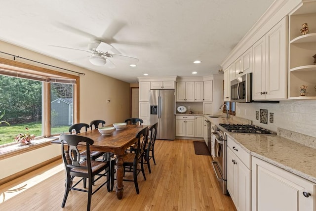kitchen with ceiling fan, open shelves, appliances with stainless steel finishes, a sink, and light wood finished floors