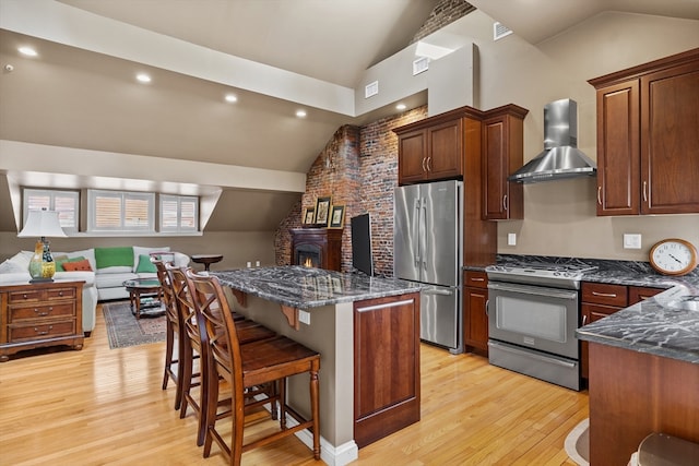 kitchen with vaulted ceiling, a kitchen breakfast bar, stainless steel appliances, light hardwood / wood-style floors, and wall chimney range hood