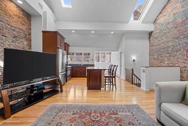 living room with brick wall, visible vents, light wood-type flooring, and lofted ceiling with skylight