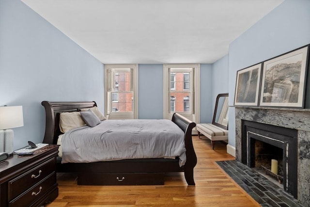 bedroom with baseboards, a premium fireplace, and wood finished floors