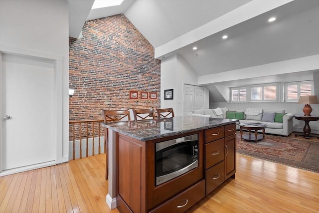 kitchen featuring stainless steel microwave, brick wall, open floor plan, light wood-style floors, and high vaulted ceiling