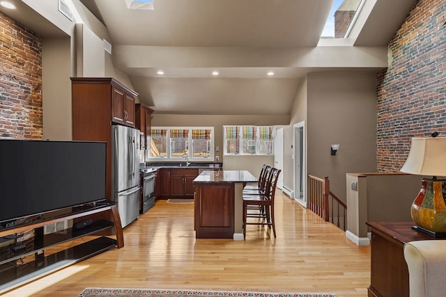 kitchen with a kitchen island, brick wall, appliances with stainless steel finishes, a breakfast bar, and light hardwood / wood-style floors