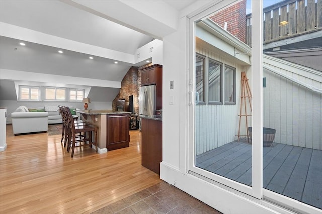 kitchen featuring open floor plan, freestanding refrigerator, a breakfast bar, light wood finished floors, and vaulted ceiling