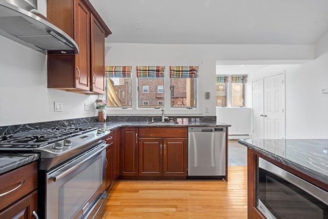 kitchen featuring a sink, appliances with stainless steel finishes, dark stone counters, and extractor fan