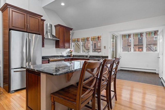 kitchen with wall chimney range hood, appliances with stainless steel finishes, light wood finished floors, a kitchen island, and lofted ceiling