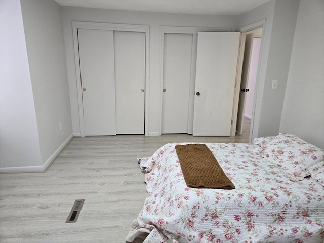 bedroom with two closets and light hardwood / wood-style flooring