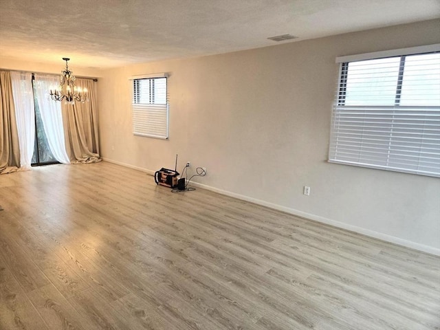 empty room with a textured ceiling, a chandelier, and light wood-type flooring