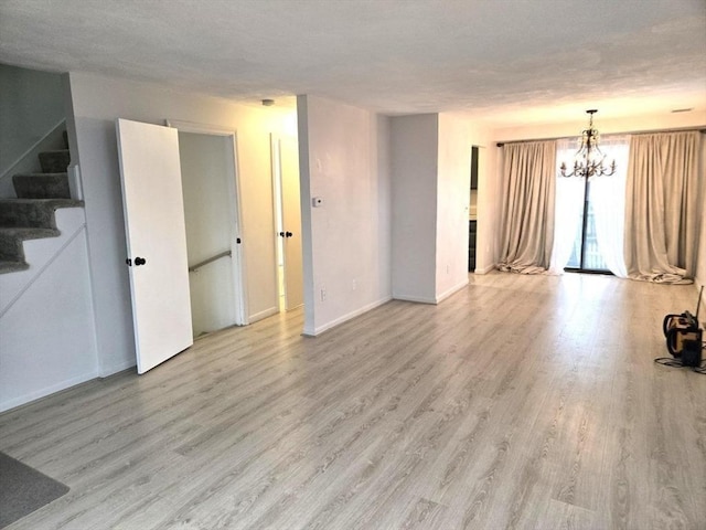 unfurnished living room with light hardwood / wood-style flooring, a textured ceiling, and a notable chandelier