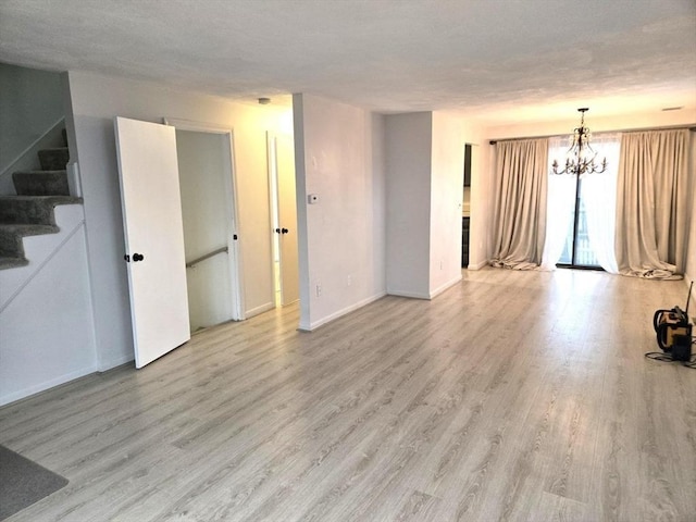 unfurnished living room featuring light wood-type flooring, an inviting chandelier, and a textured ceiling