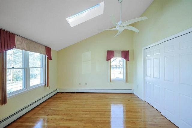 unfurnished bedroom with lofted ceiling with skylight, multiple windows, light wood-type flooring, and a baseboard radiator