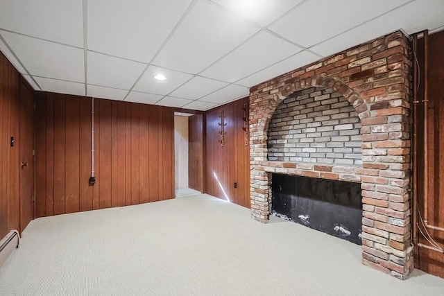 unfurnished living room with carpet floors, recessed lighting, a paneled ceiling, wood walls, and a brick fireplace