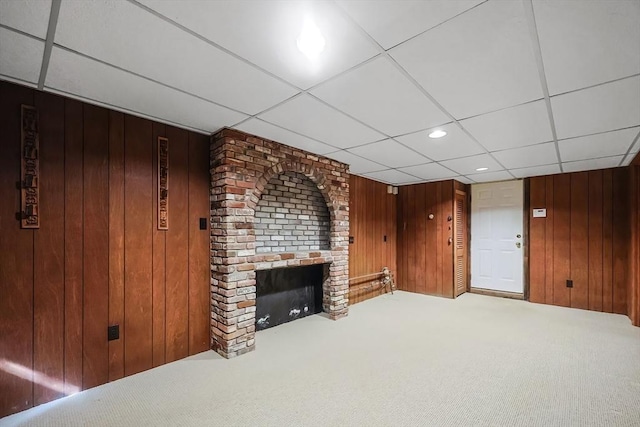 carpeted living area featuring a brick fireplace, a paneled ceiling, and wood walls