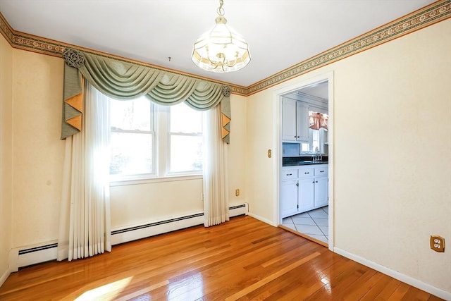 spare room with a sink, a baseboard radiator, baseboards, and light wood-style floors