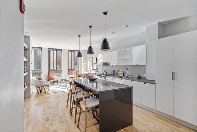 kitchen featuring white cabinetry, decorative light fixtures, a kitchen island, and light hardwood / wood-style flooring