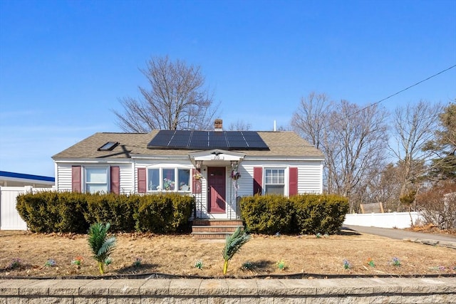 view of front of property with solar panels, a chimney, and fence