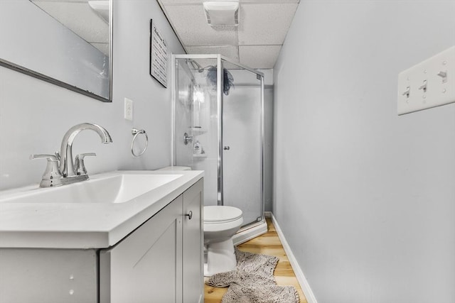 bathroom featuring a drop ceiling, a stall shower, toilet, and vanity