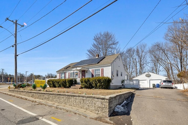 view of front facade with an outbuilding, roof mounted solar panels, a detached garage, a shingled roof, and a chimney