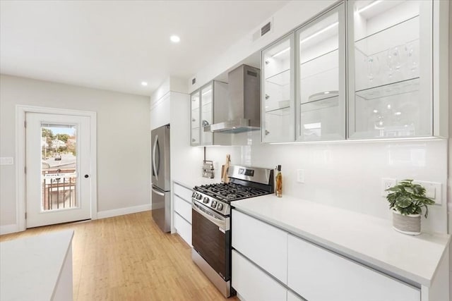 kitchen featuring white cabinets, light hardwood / wood-style flooring, wall chimney range hood, and appliances with stainless steel finishes