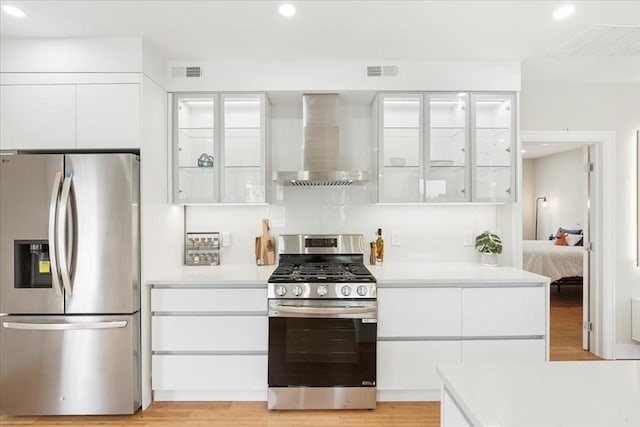 kitchen with light hardwood / wood-style floors, white cabinetry, wall chimney range hood, and appliances with stainless steel finishes