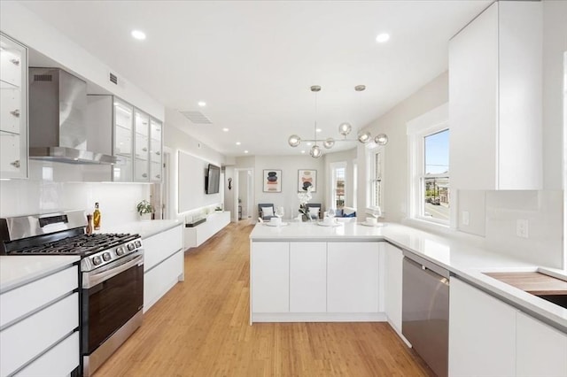 kitchen featuring appliances with stainless steel finishes, hanging light fixtures, decorative backsplash, white cabinets, and wall chimney exhaust hood