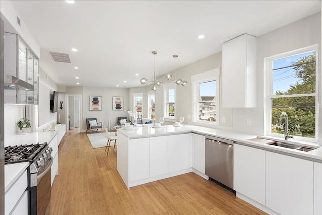 kitchen with appliances with stainless steel finishes, white cabinets, sink, kitchen peninsula, and pendant lighting