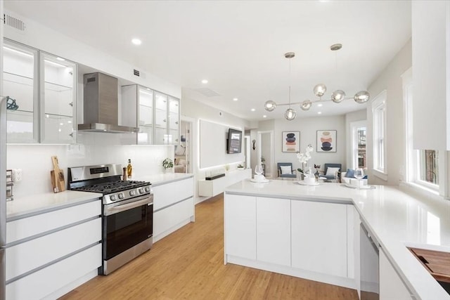 kitchen with light hardwood / wood-style flooring, hanging light fixtures, appliances with stainless steel finishes, wall chimney exhaust hood, and white cabinets