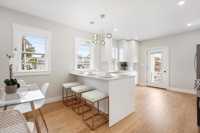 kitchen with white cabinets, decorative light fixtures, light wood-type flooring, kitchen peninsula, and a breakfast bar