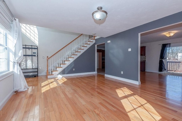 unfurnished living room featuring stairs, baseboards, and wood finished floors