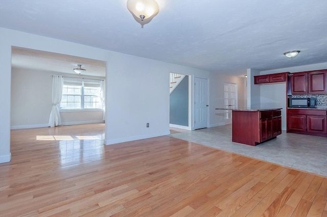 kitchen with open floor plan, dark brown cabinets, light wood finished floors, and black microwave