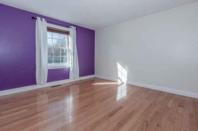 empty room featuring light wood-style flooring, visible vents, and baseboards